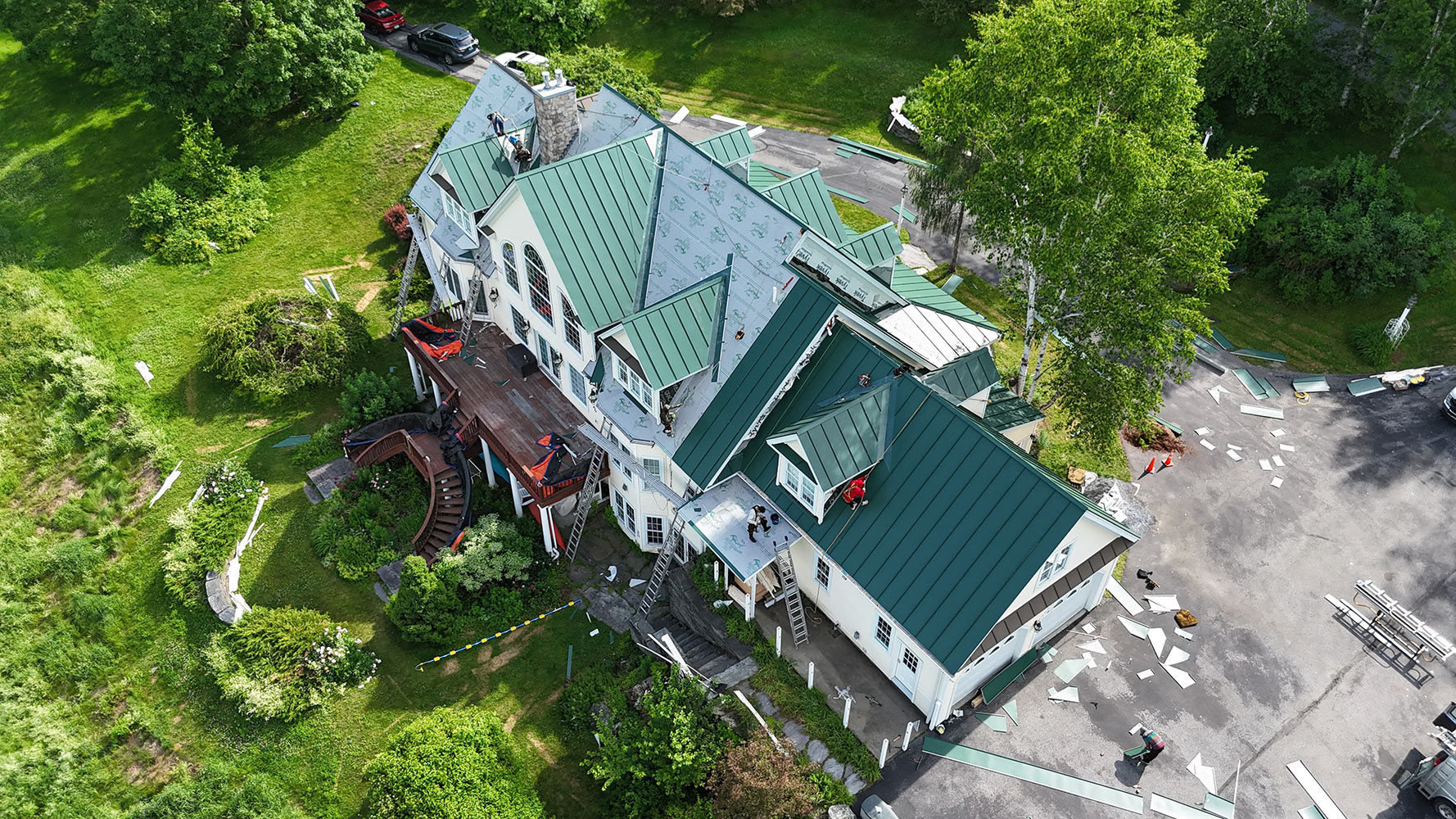 During — 24-gauge Englert forest green standing seam panels being installed on Waterbury Vermont estate with Sharkskin underlayment visible on unfinished sections