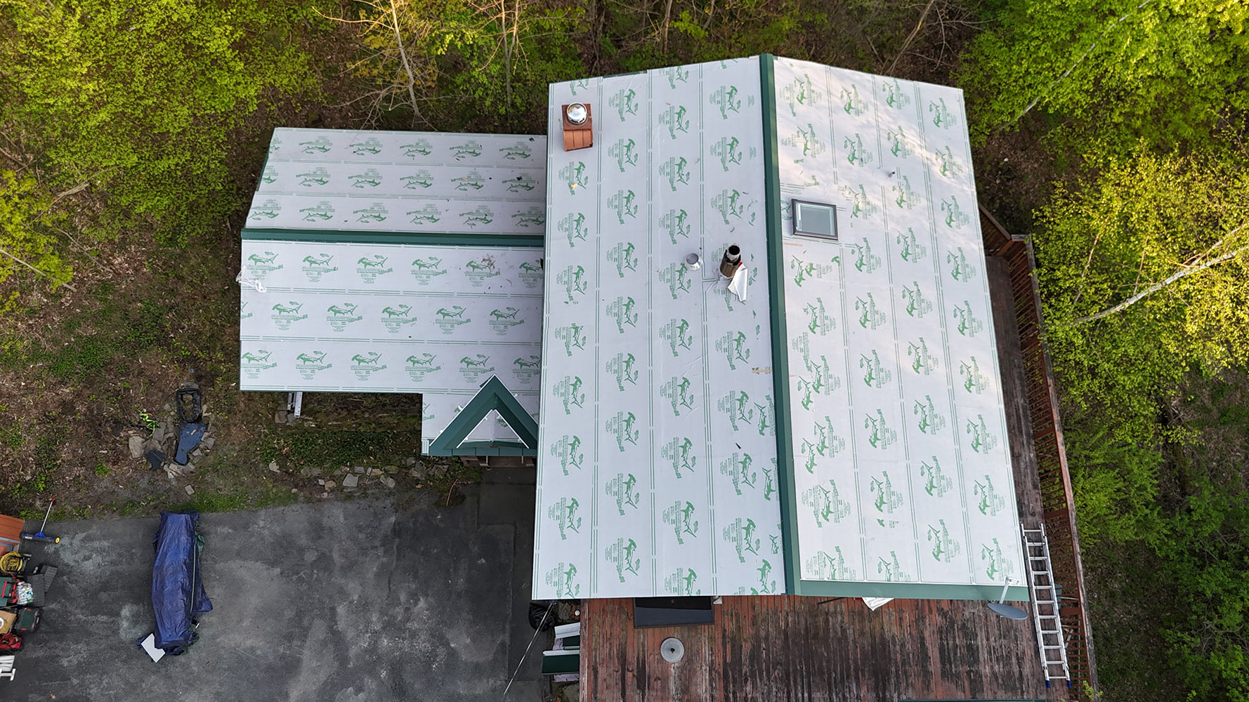 Overhead drone view during standing seam installation — metal roofing underlayment covering Stowe Vermont home, green trim visible