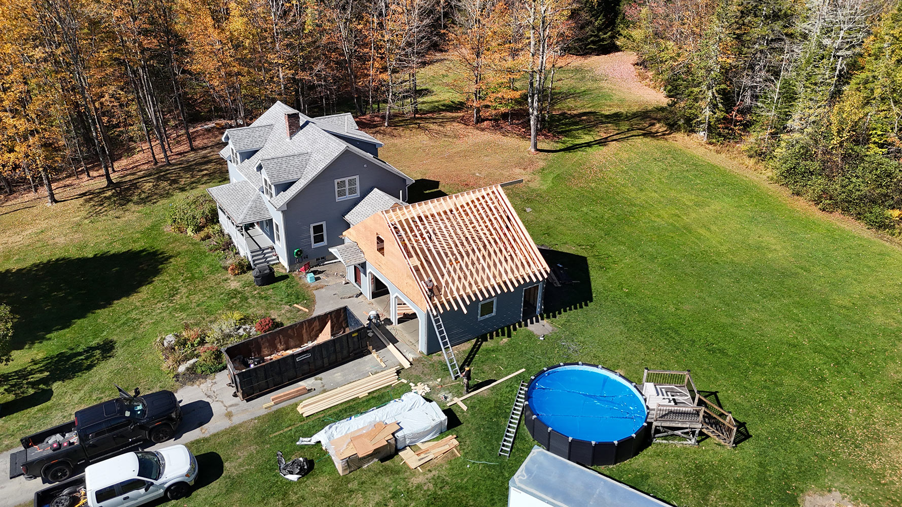 Roofing crew installing shingles on new construction garage addition in Stowe Vermont — aerial fall foliage