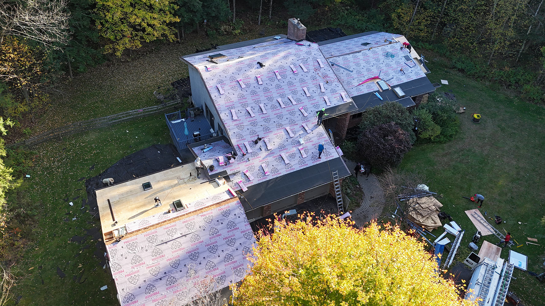 Aerial view of roofing crew installing ProArmor underlayment on large Williston Vermont home — fall foliage