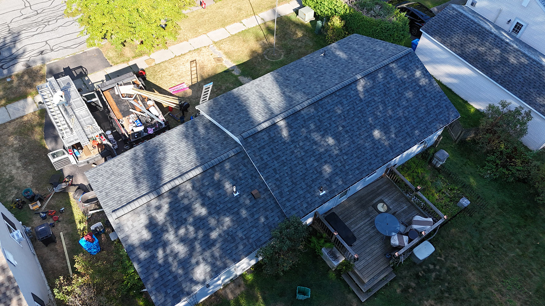 Completed roof replacement Burlington Vermont North End — angled aerial view showing both roof planes, cleanup truck still on site, Rivers Construction