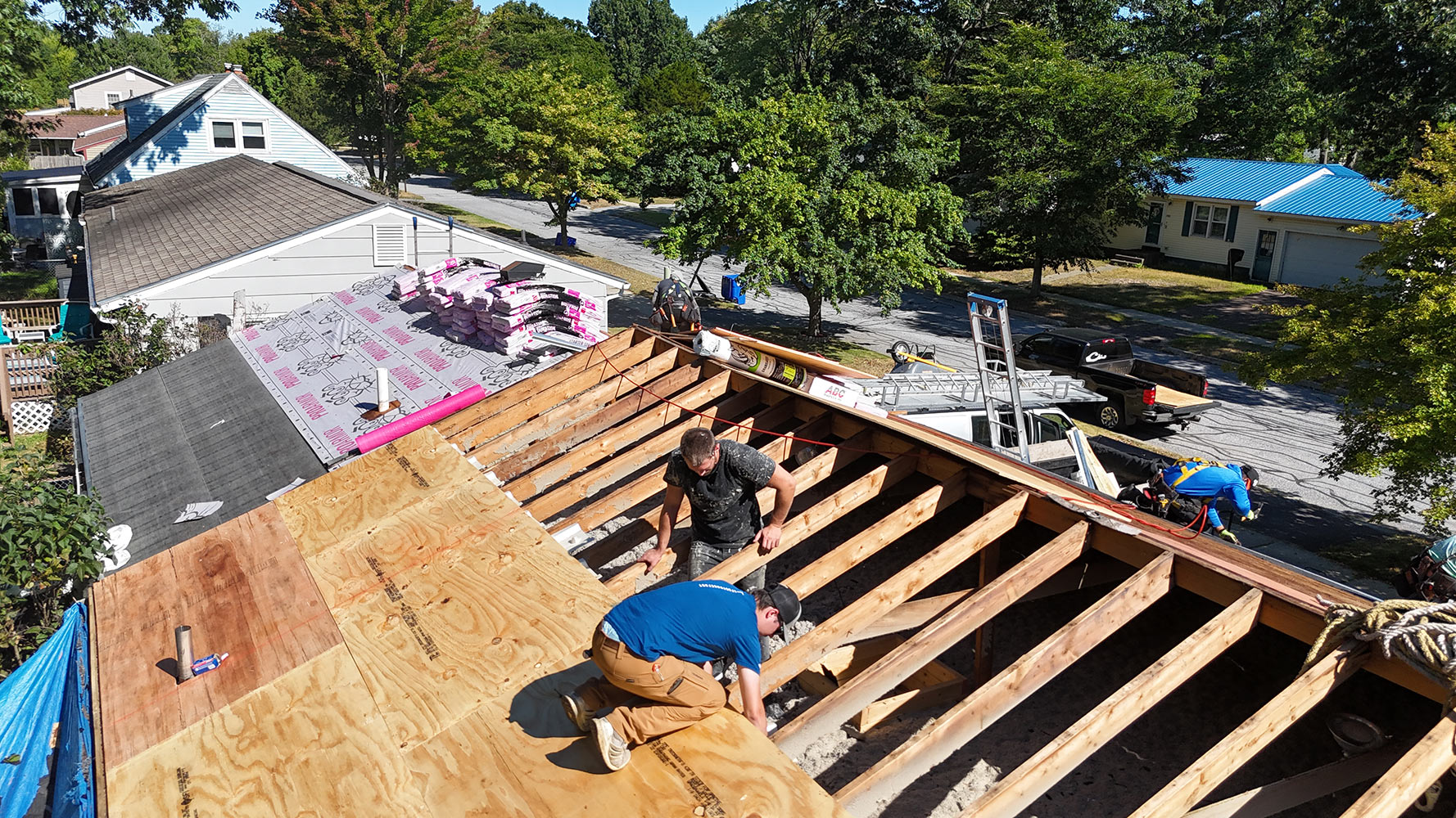 Rivers Construction crew installing new roof deck sheathing on a Burlington Vermont home — two workers fitting plywood panels on exposed rafters, active job site