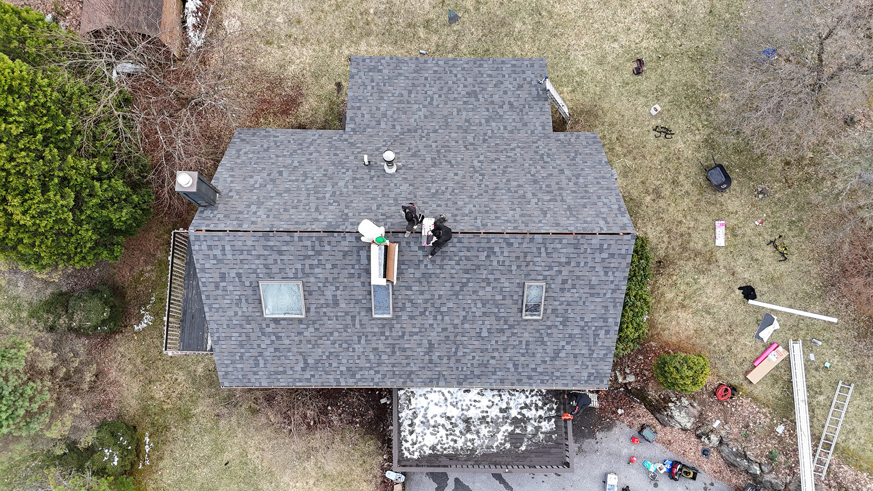 Overhead drone view of roofing crew installing ridge cap on Richmond Vermont shingle replacement — skylights visible from above