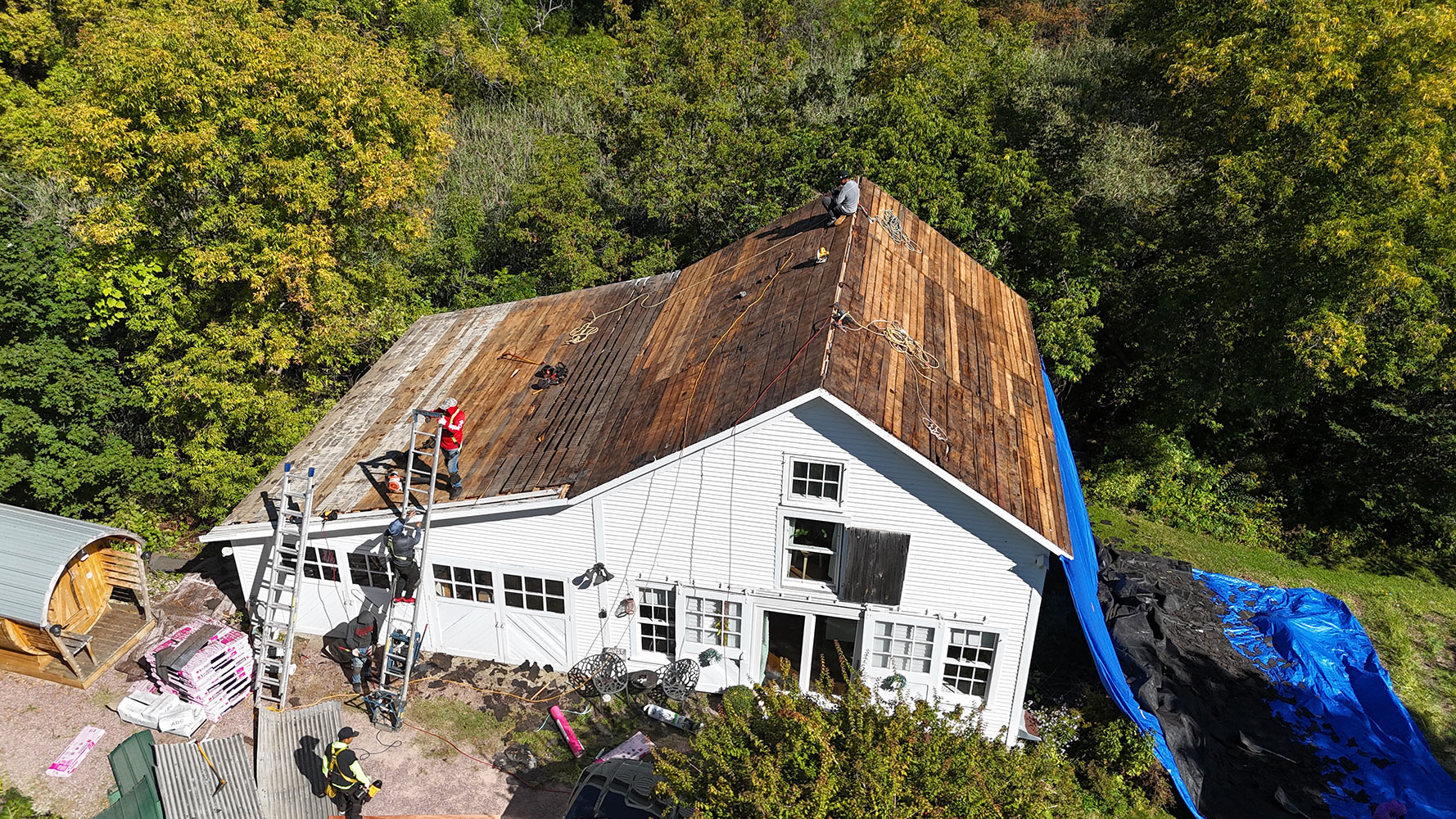 Crew tearing off old shingles on Williston Vermont farmhouse — bare wood plank sheathing exposed, angled aerial view